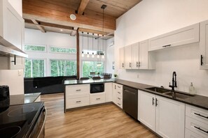 A modern kitchen with white cabinetry, a black countertop, and a wooden ceiling.