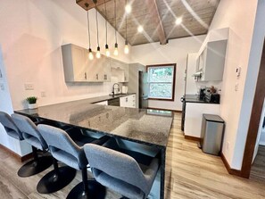 A modern kitchen with a central island, bar stools, pendant lighting, and a view of the outdoors.