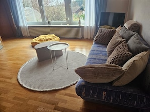A living room with a sofa, a round table, a yellow bean bag, and a view through a window. - Apartment 'Haus  Am Goldberg' with Mountain View, Private Terrace and Wi-Fi (Tannheim)