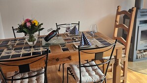 Een eetgedeelte met een houten tafel, stoelen, een vaas met bloemen, een schilderij aan de muur en een open haard.