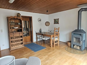 A cozy living room with a wooden ceiling, a dining area with a table and chairs, a built-in wood stove, and a wine rack. - Apartment 'Haus  Am Goldberg' with Mountain View, Private Terrace and Wi-Fi (Tannheim)