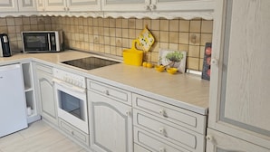 Een keuken met witte kasten, een magnetron, een spoelbak en een gele fruitschaal.