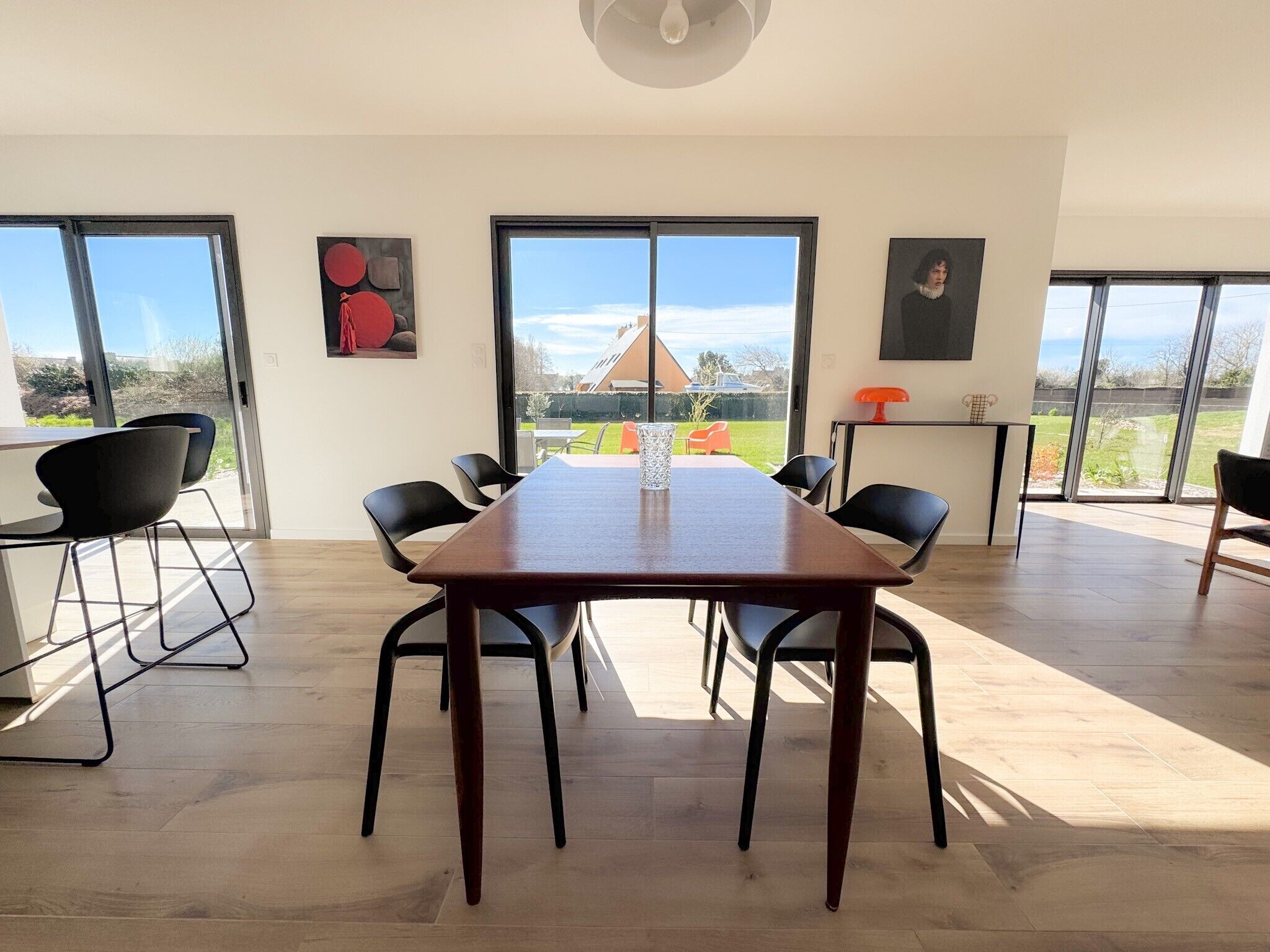 Une salle à manger moderne avec une grande table, des chaises noires et de grandes fenêtres donnant sur l’extérieur.