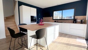 A modern kitchen with a wooden island, black chairs, and a large window. - Ty Nevez – Holiday Home with Private Terrace, Garden & Wi-Fi in Penmarch (Penmarch)