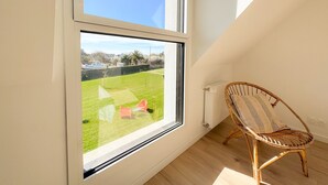 A room with a large window, a wicker chair, and a radiator. - Ty Nevez – Holiday Home with Private Terrace, Garden & Wi-Fi in Penmarch (Penmarch)
