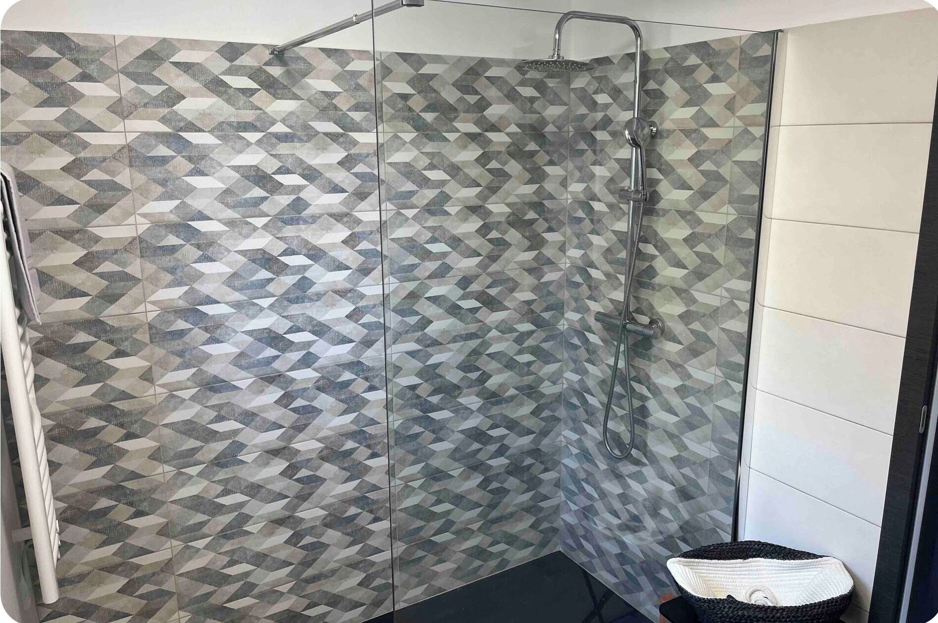 Una ducha con un patrón geométrico de azulejos y puerta de cristal.