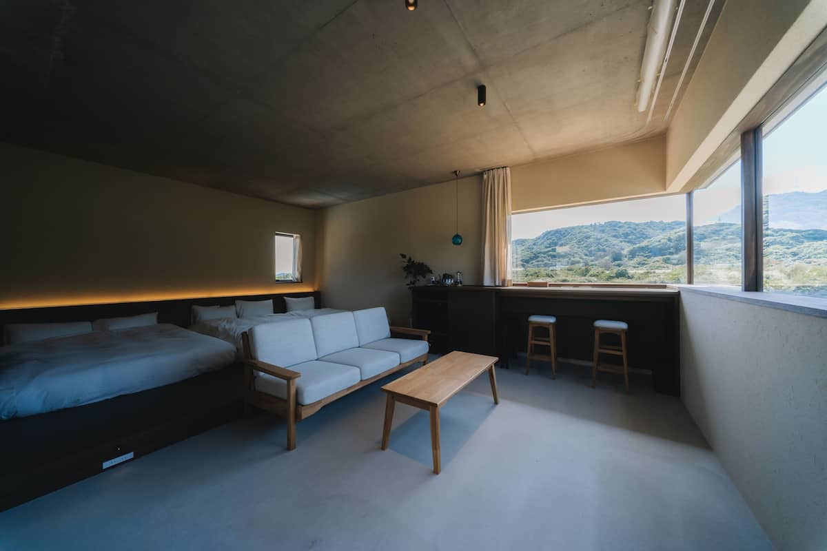 A modern room with a bed, sofa, and a small dining area with stools.