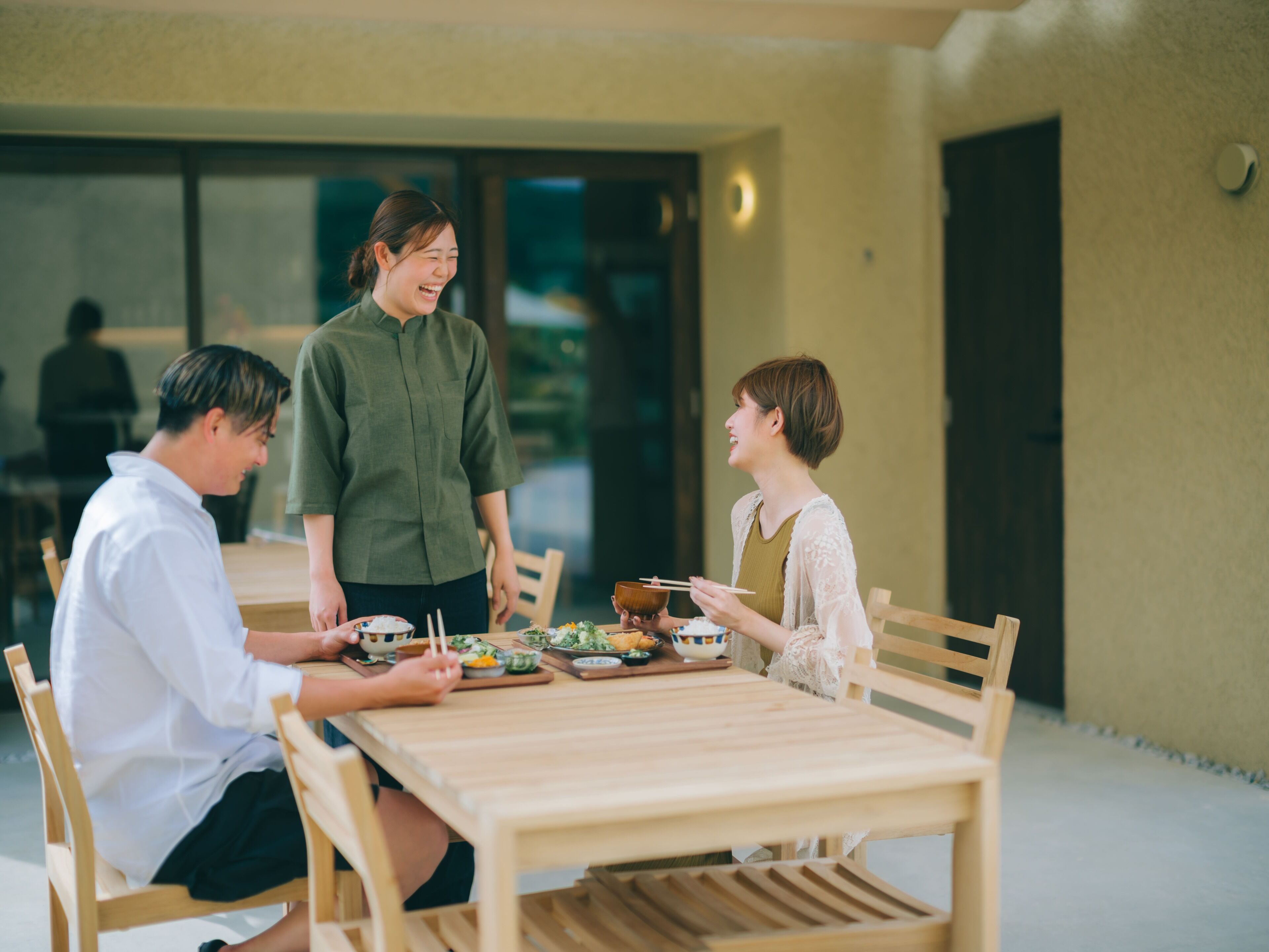A wooden table with chairs, a person standing, and another person seated.