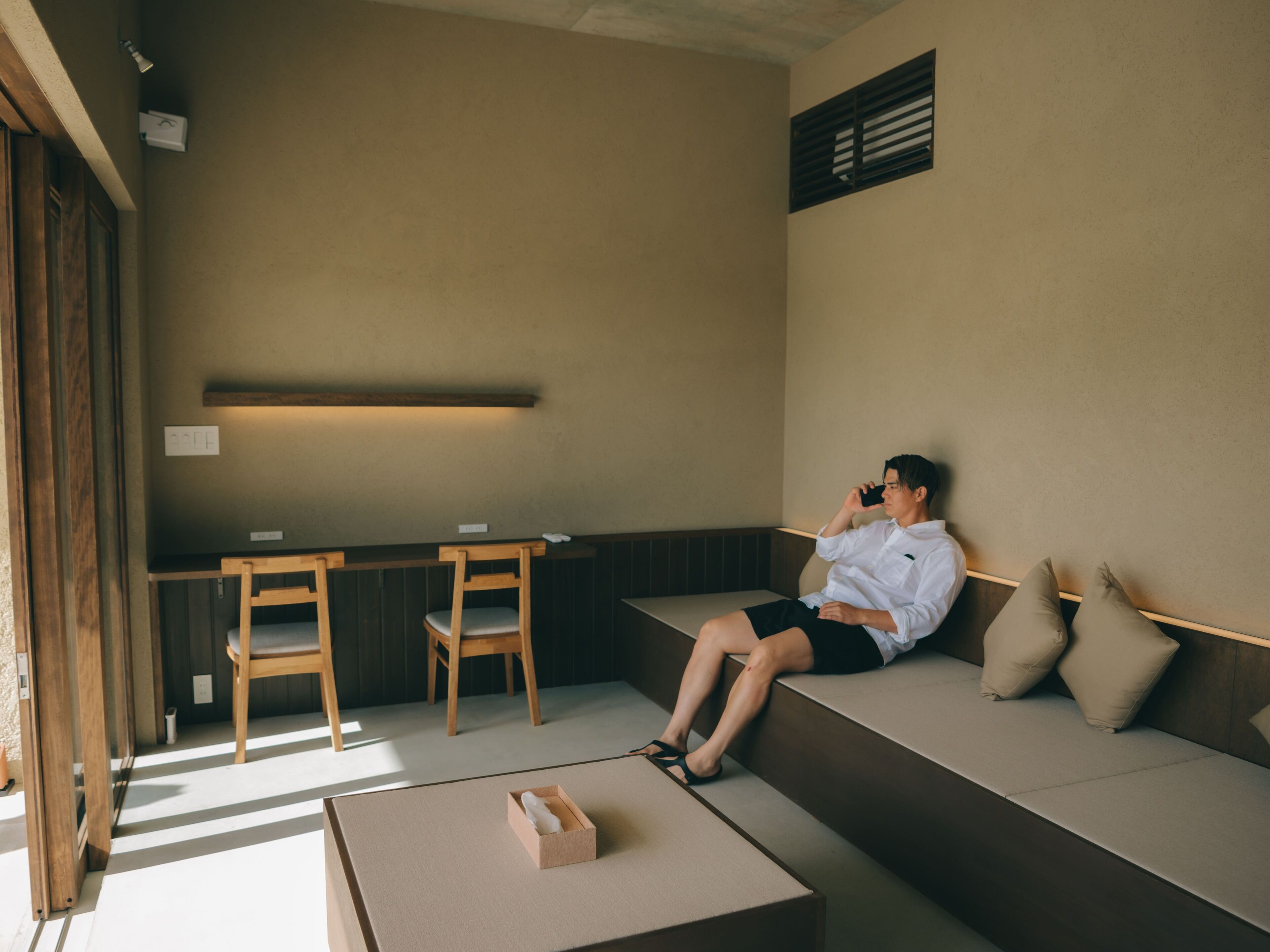 A man sitting on a bench in a room with a low table and chairs.