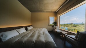 Ein Schlafzimmer mit einem großen Bett, einem Schreibtisch, einem Stuhl und einem Fenster mit Blick auf Grünflächen.