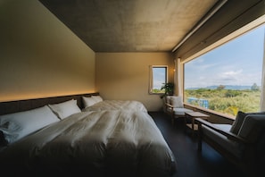 Un dormitorio con una cama grande, un escritorio, una silla y una ventana con vistas a zonas verdes.