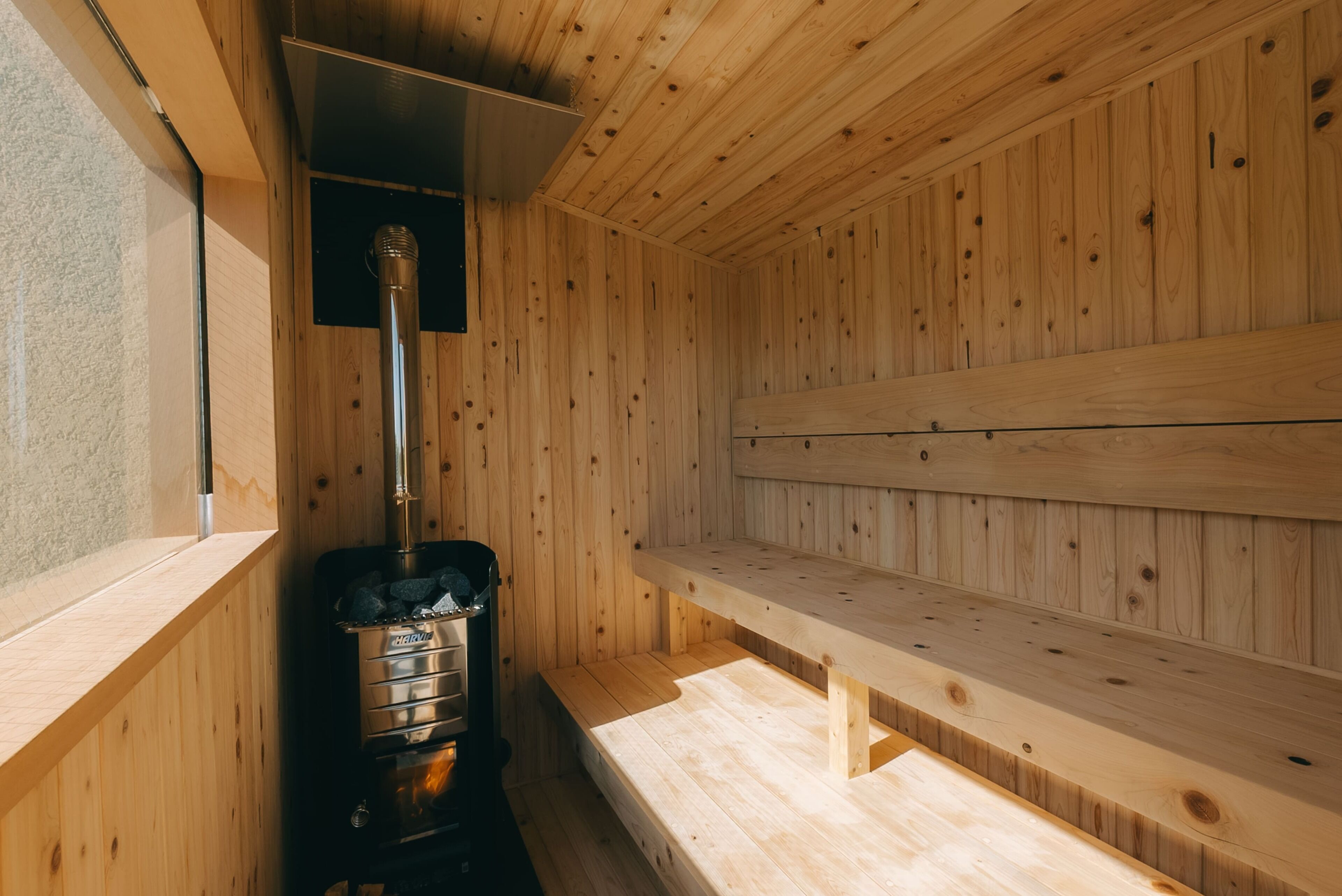 Una sauna con paredes y bancos de madera, un generador de vapor y una ventana.