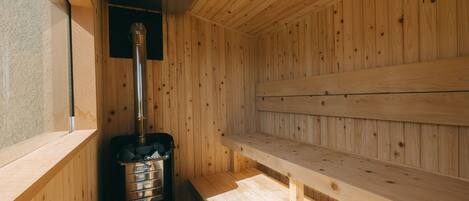 Una sauna con paredes y bancos de madera, un generador de vapor y una ventana.