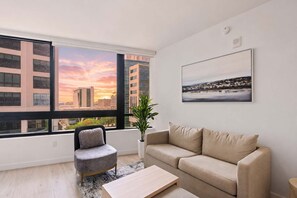 A modern living room with a large window, a sofa, a chair, and a coffee table. - 1BR | Walk to Bayside | Rooftop Pool & Gym (Miami)