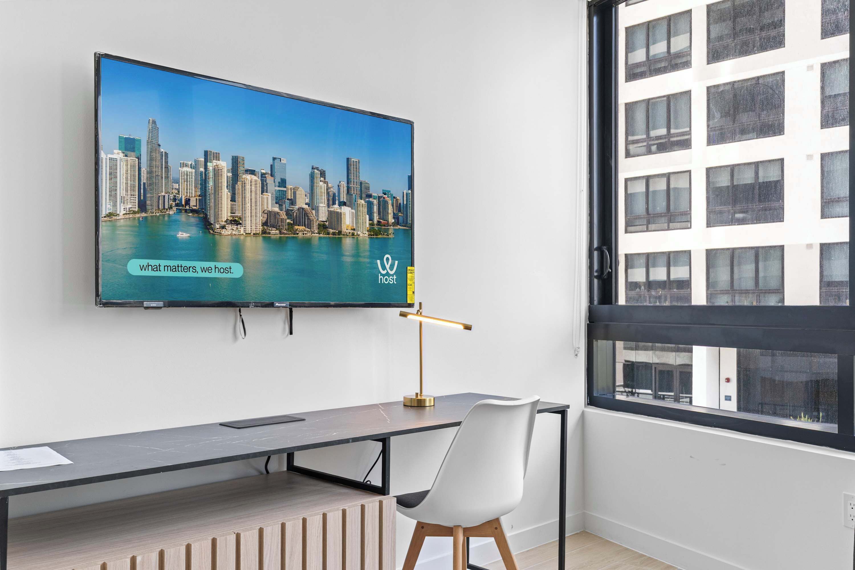A modern office space with a large flat-screen TV displaying a cityscape, a desk with a lamp, and a chair.