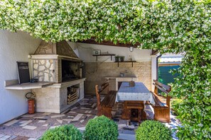 An outdoor patio with a stone fireplace, wooden benches, and a table. - Sea Breeze Funtana Studio Apartment A10 (Funtana)
