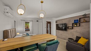 Een moderne woonkamer met een houten eettafel, twee stoelen, een bank en een aan de muur bevestigde televisie.