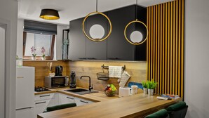 Een moderne keuken met een houten aanrecht, een spoelbak, een fornuis en een magnetron. Twee hanglampen, een raam met zonwering en een houten paneel aan de muur.