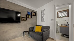 Een moderne woonkamer met een grijze bank, een flatscreen televisie en een klein krukje.