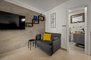 A modern living room with a grey sofa, a flat-screen TV, and a small stool. - Sea Breeze Funtana Studio Apartment A10 (Funtana)