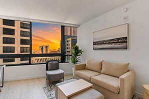 A modern living room with a large window, a sofa, a chair, a coffee table, and a cityscape view. - 1-Bed | Metromover & Brightline Access (Miami)