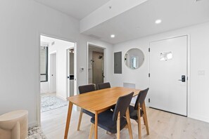 A modern room with a wooden dining table, chairs, a round mirror, and a white door. - 1-Bed | Metromover & Brightline Access (Miami)
