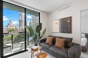 A modern living room with a grey sofa, a coffee table, and a view of a cityscape through large windows. - Luxury 2BR | Free Parking | Walk to FIFA Fan Fest (Miami)