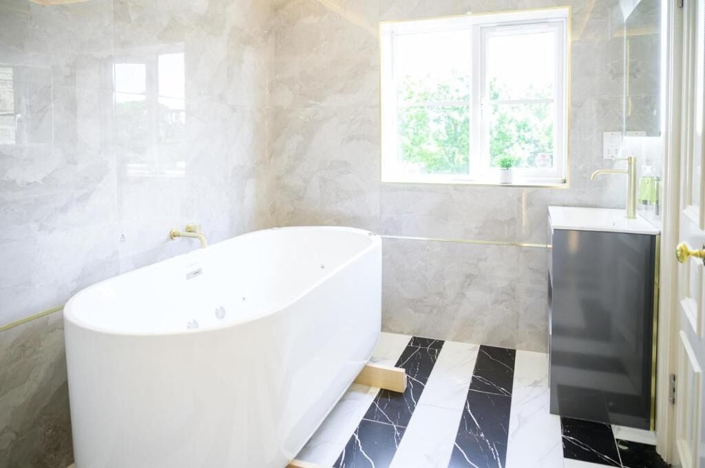 A modern bathroom with a freestanding bathtub, a window with a view of greenery, and a marble floor.