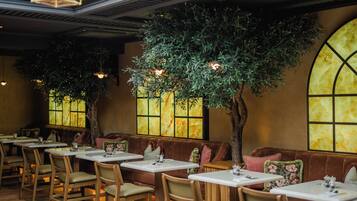 A restaurant interior with wooden tables and chairs, a large tree, and a stained glass window.