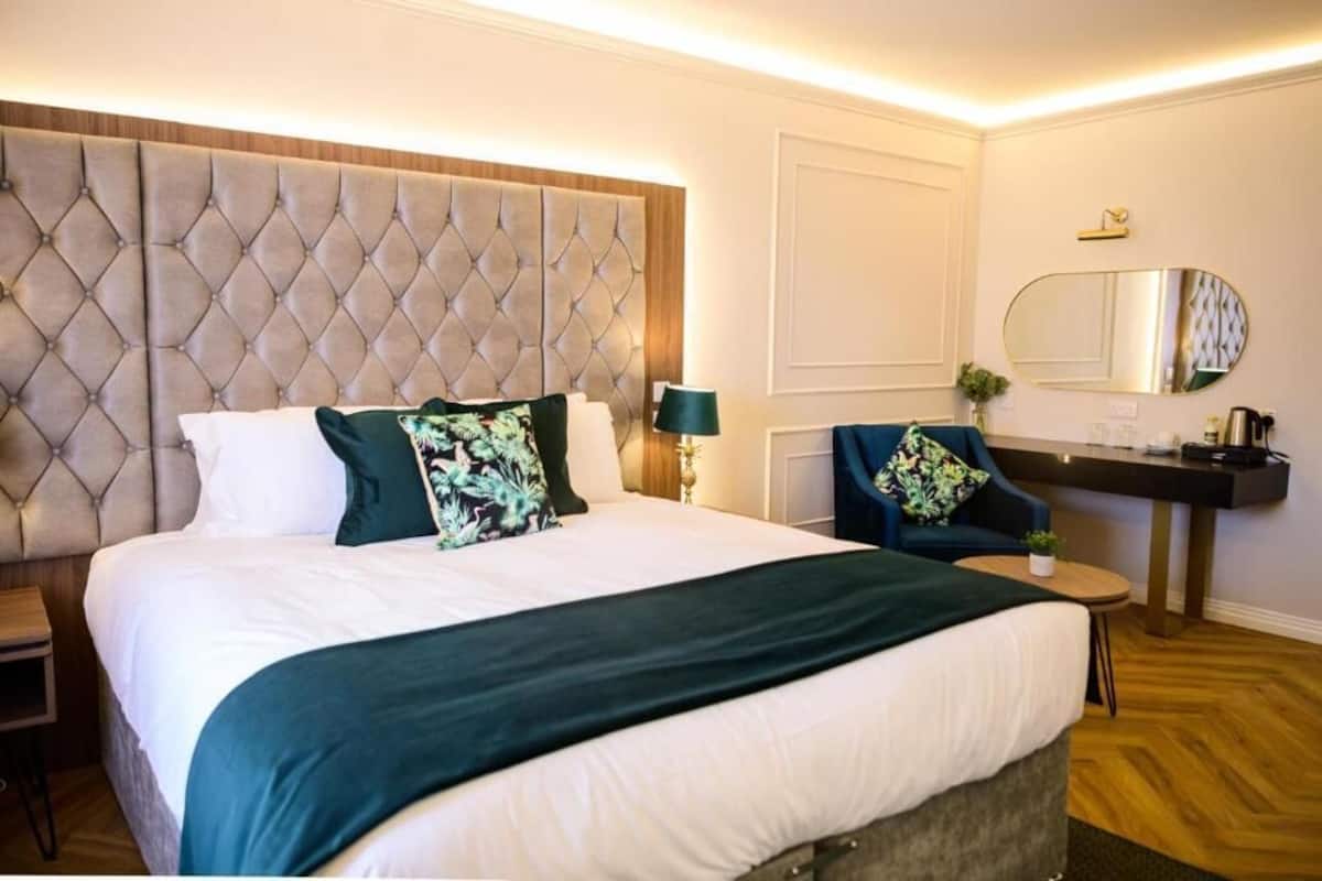 Ein Hotelzimmer mit einem großen Bett, einem Schreibtisch, einem Sessel, einem Spiegel und einem kleinen Tisch.