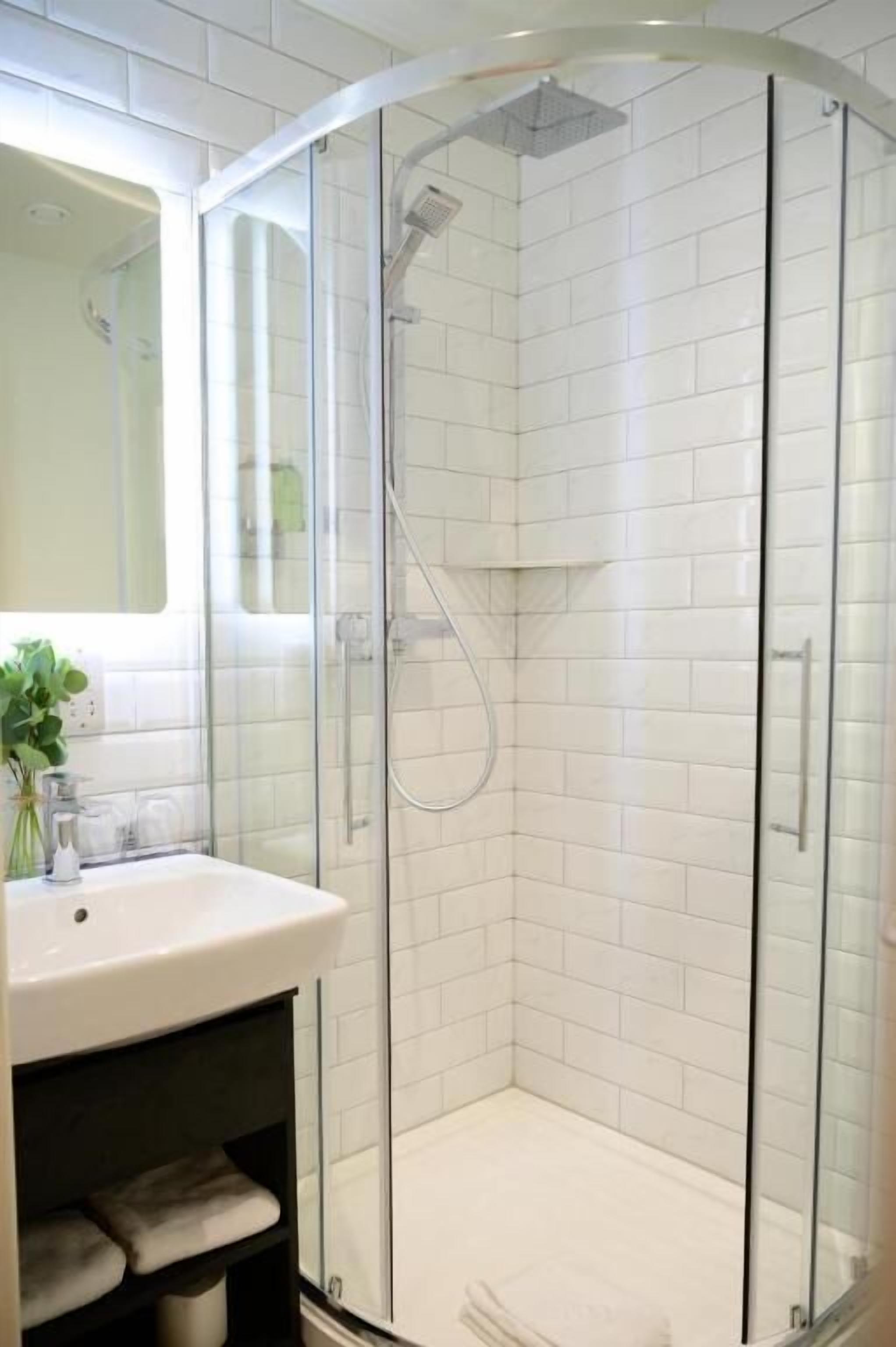 A modern bathroom with a glass-enclosed shower, white tiled walls, and a white sink.