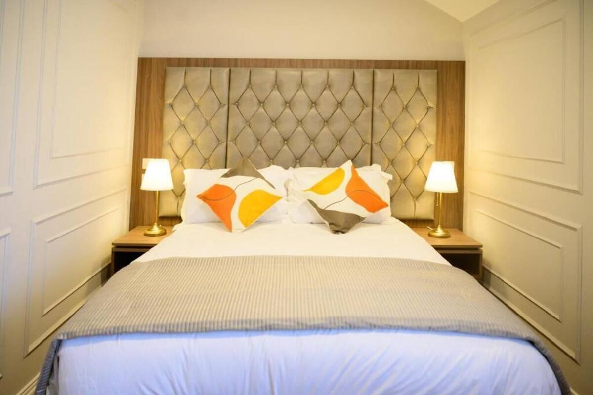 Ein Hotelzimmer mit einem gepolsterten Kopfteil, einem großen Bett mit gestreifter Bettdecke, zwei Nachttischlampen und einem Nachttisch.
