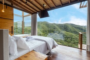 A bedroom with a large window, wooden ceiling, and a bed with white linens.