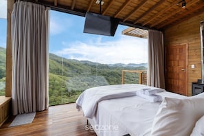 A bedroom with a large bed, wooden flooring, a TV, and a view of green hills. - Cabin With Fantastic View and Jacuzzi Vst029 (Anitapolis)