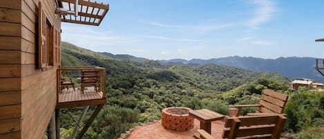 Une terrasse en bois avec un foyer en briques, des chaises en bois et une table offrant une vue sur un paysage montagneux.