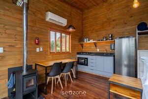 A wooden cabin interior with a kitchen, dining area, and a wood stove.