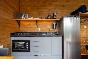 Eine kompakte Küche mit Einbauofen, Kühlschrank und Kaffeemaschine auf einer Holzwandablage.