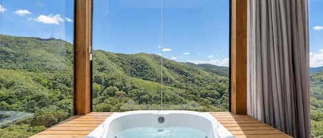 Un jacuzzi en una terraza de madera con una vista panorámica de colinas verdes y cielo despejado.