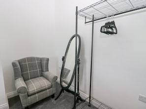 A room with a grey plaid sofa, a metal drying rack with clothes, and a mirror. - Victroneen Cottage (Whitehaven)