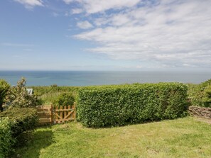 Un paysage côtier avec une haie, un portail en bois et une vue sur la mer.