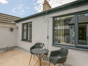 A patio with a table and two chairs, a window, and a chimney. - Victroneen Cottage (Whitehaven)