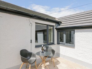 Une petite terrasse avec deux chaises et une table, une fenêtre et une prise de courant.