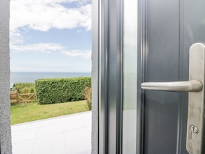 A door with a view of a grassy area and a hedge, leading to a patio with a tiled floor. - Victroneen Cottage (Whitehaven)