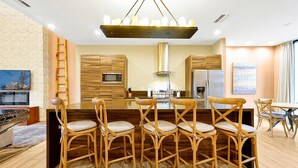 A modern kitchen with wooden cabinets, a central island with bar stools, a built-in microwave, and a stainless steel refrigerator. - Spacious Luxury 4BR Suite Near Disney (Kissimmee)
