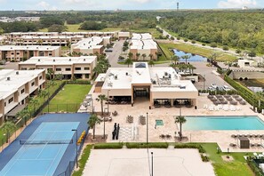 Un hotel con varias edificaciones, piscina, canchas de tenis y un área ajardinada con palmeras.