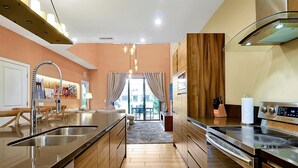 A modern kitchen with a central island, stainless steel appliances, and wooden cabinetry. - Spacious Luxury 4BR Suite Near Disney (Kissimmee)