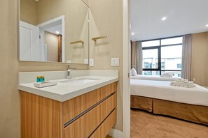 Habitación de hotel con tocador de baño blanco, cama con vistas y ventana grande.