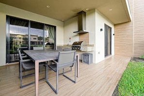An outdoor patio with a dining table and chairs, a barbecue grill, and a large window. - Spacious Luxury 4BR Suite Near Disney (Kissimmee)