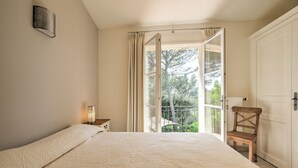 Ein Schlafzimmer mit einem Bett, einem Nachttisch, einem Sessel und einem Fenster mit Vorhängen.