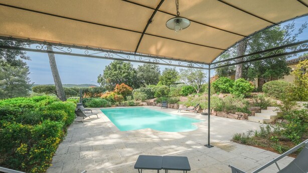 Ein überdachter Außenbereich mit Pool, Liegestühlen und einem Tisch.